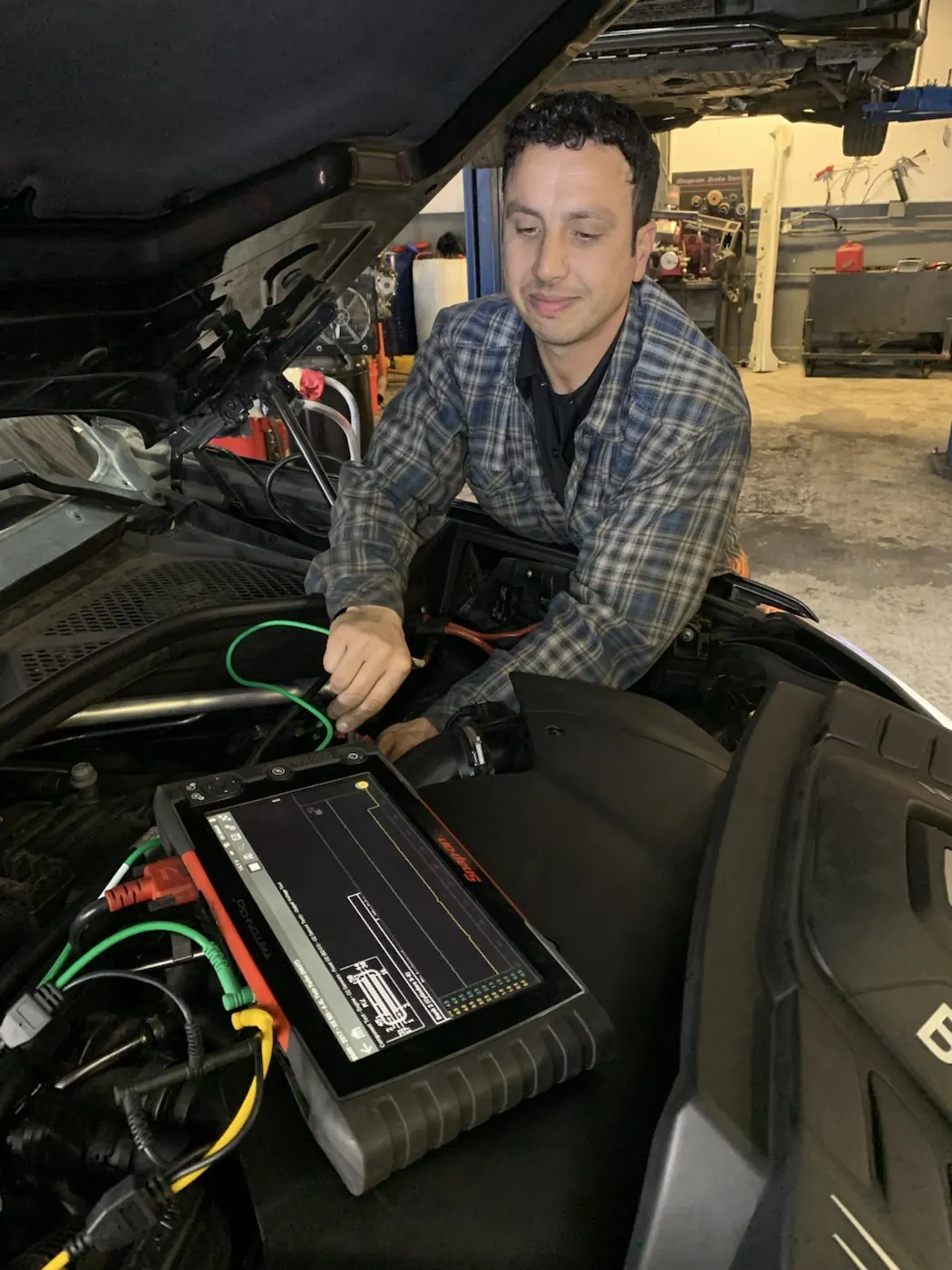 Technician performing vehicle diagnostics under the hood